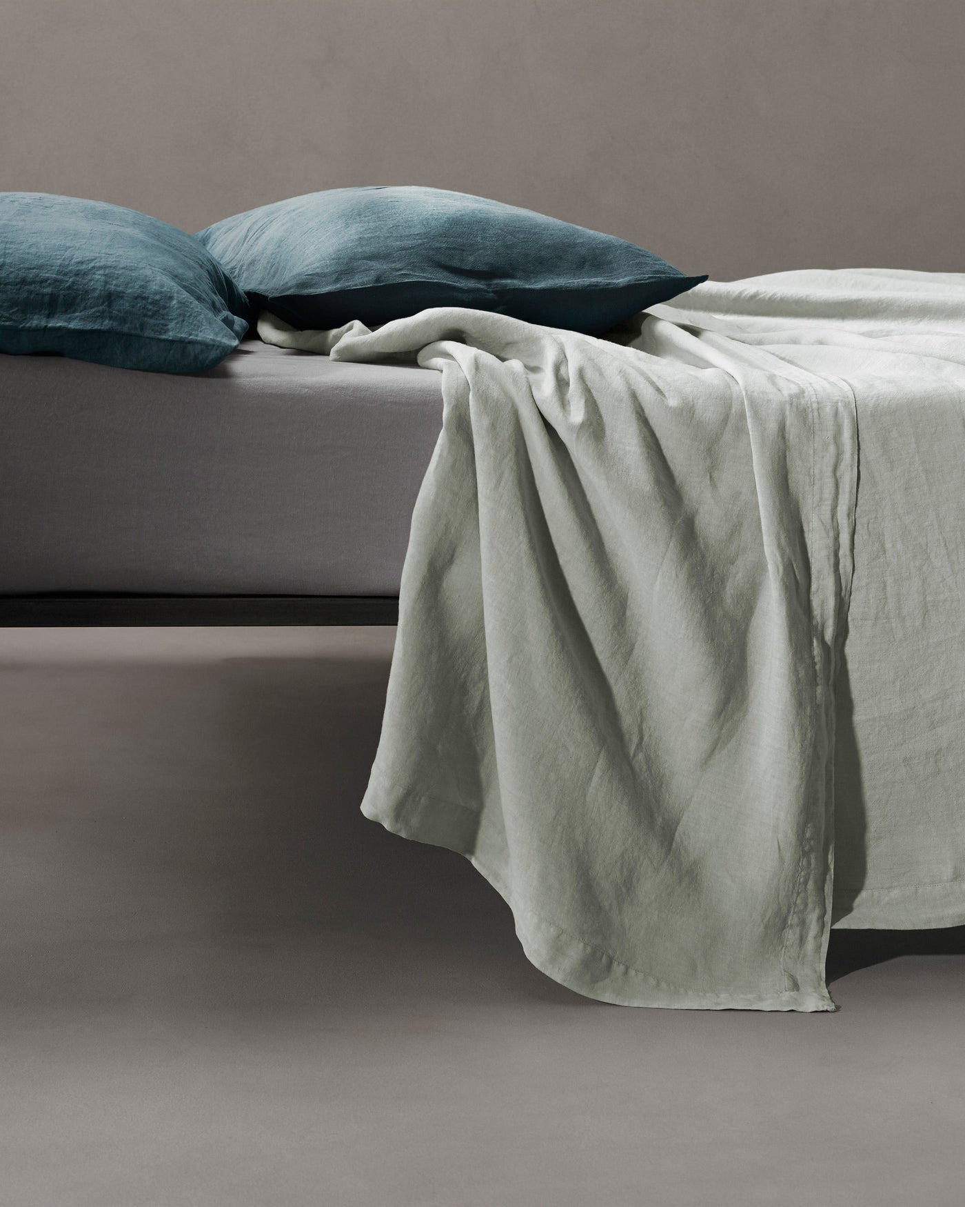 Sage linen flat sheet draped over bed edge, styled with teal pillowcases.