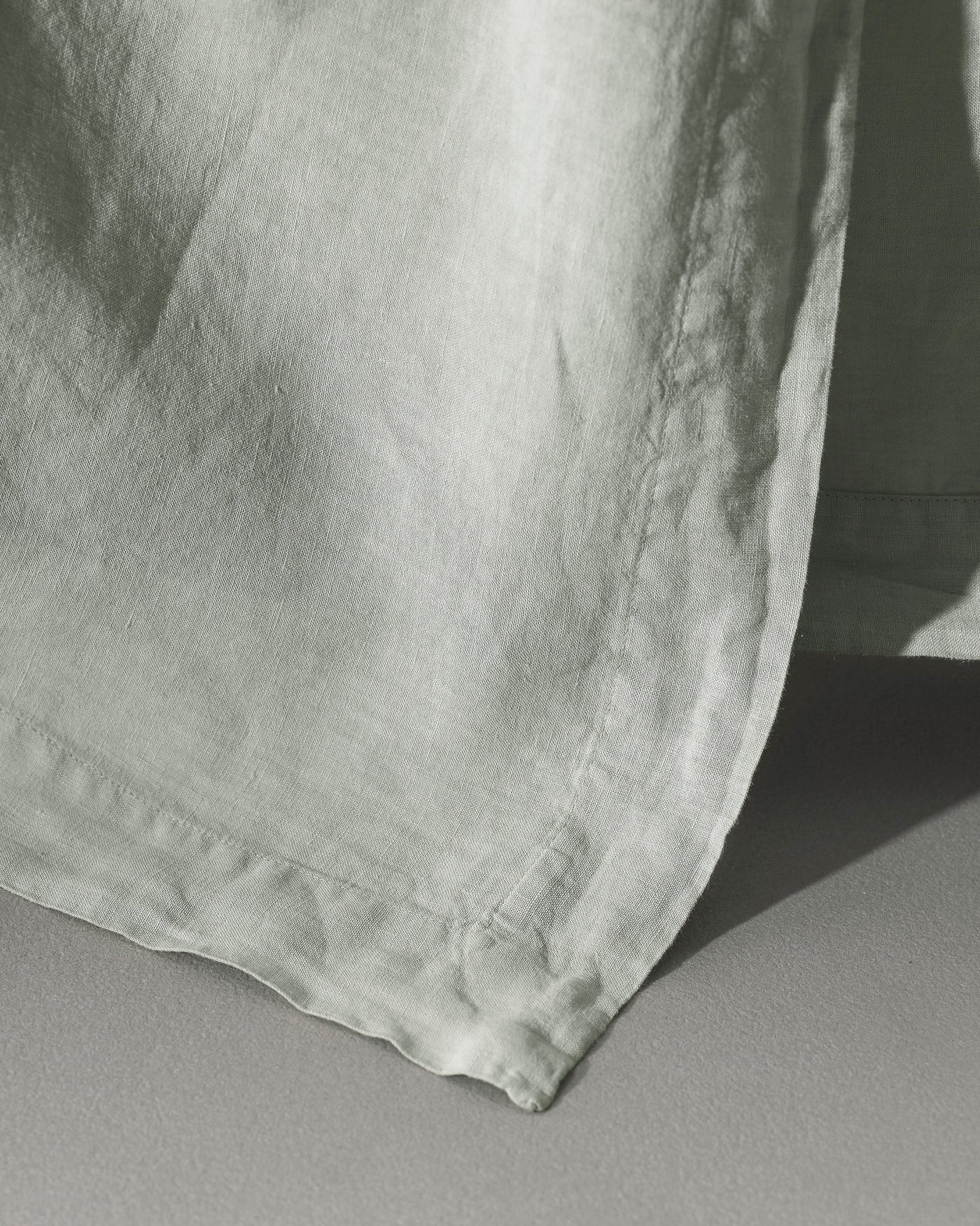 Close-up of Society Limonta Rem flat sheet hem in sage, showing washed linen texture.