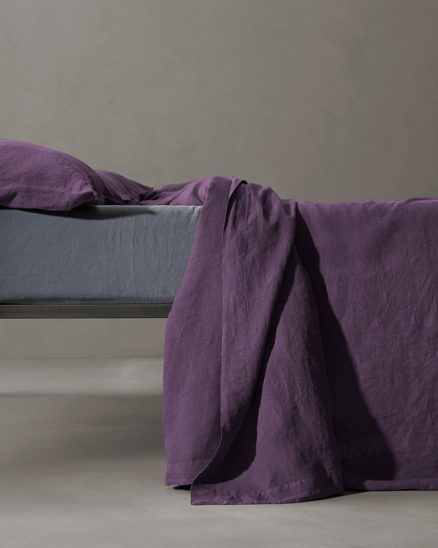 Plum linen flat sheet draped over bed edge, paired with slate fitted sheet.