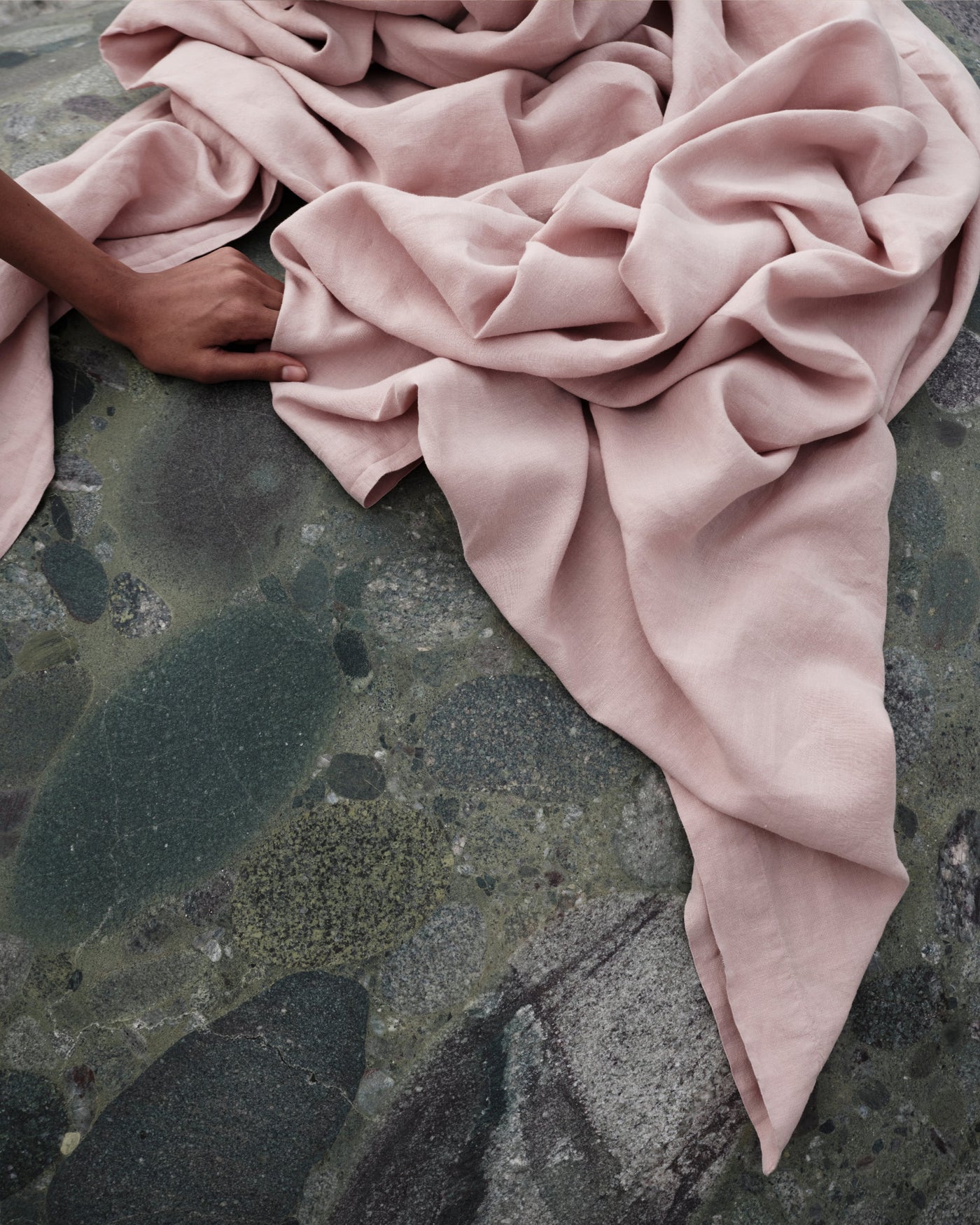 Society Limonta Rem flat sheet in blush linen, draped loosely over wet dark stone surface.