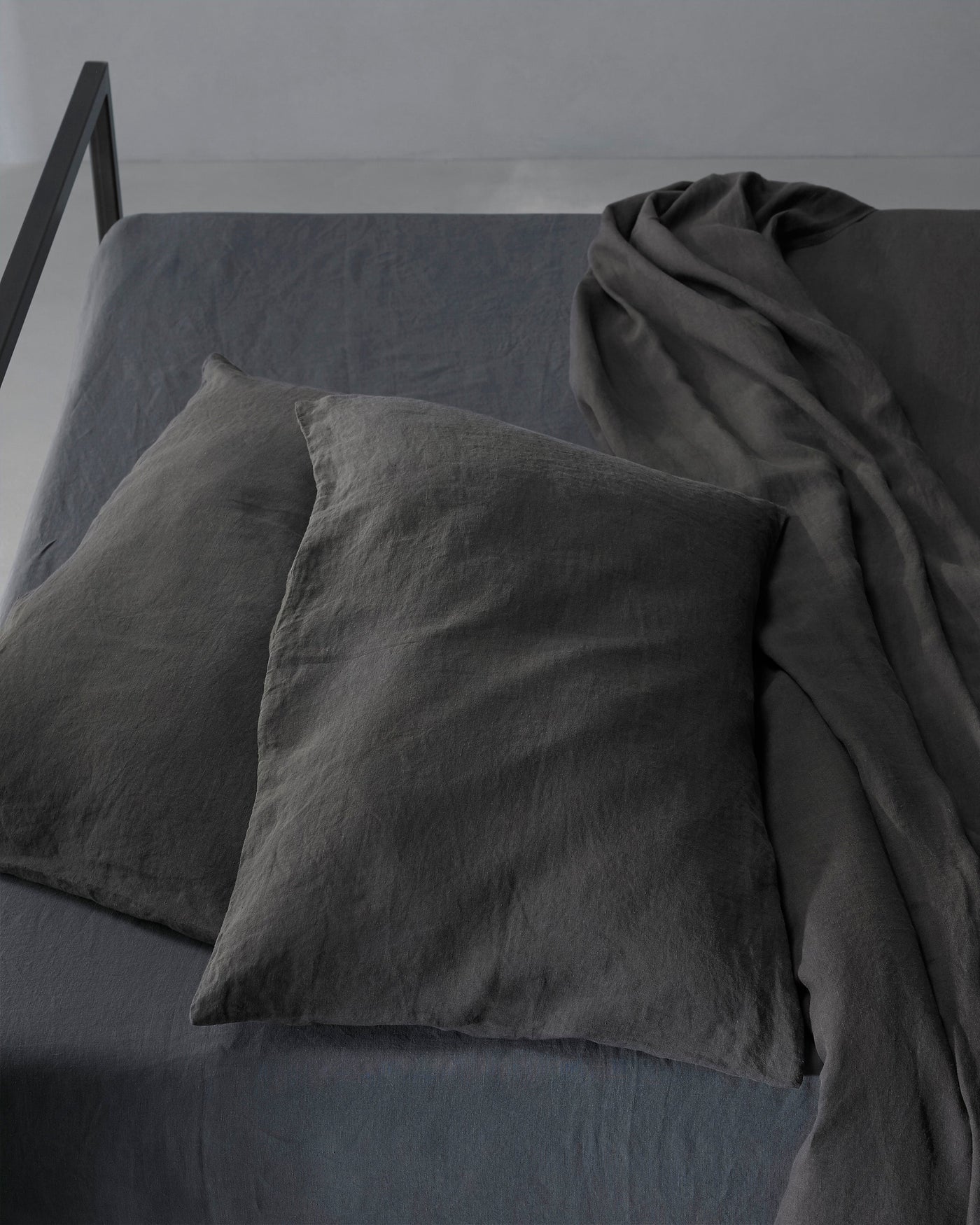 Charcoal linen pillowcases styled on a bed with matching draped sheet, overhead angle.