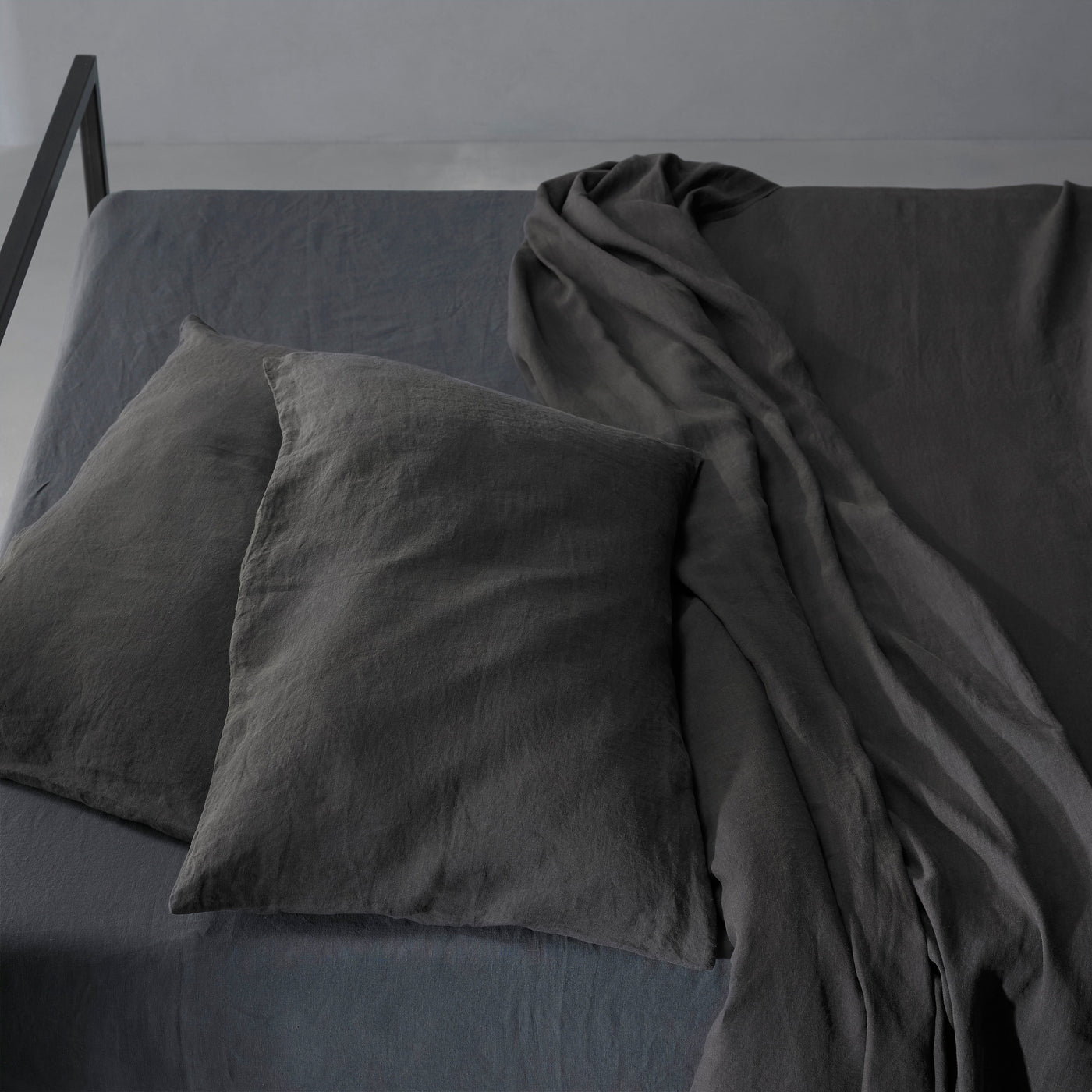 Society Limonta Rem pillowcases in charcoal linen, draped flat sheet cascading off bed edge.