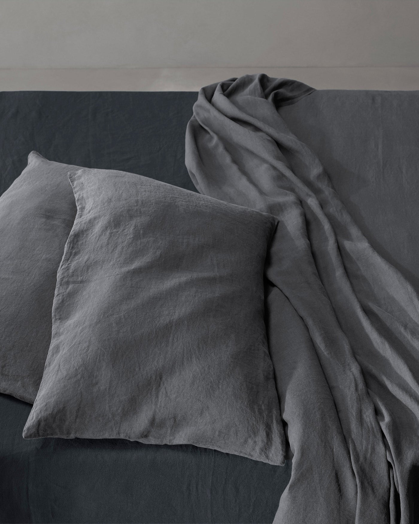 Draped charcoal linen sheet cascading over stacked Rem pillowcases on a made bed.