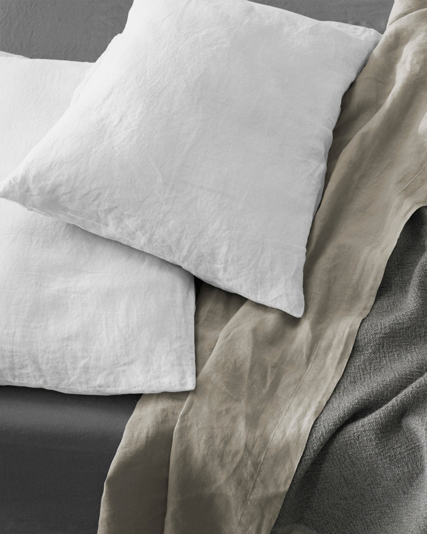 White linen pillowcases with natural texture, styled on a bed with taupe and charcoal layers.