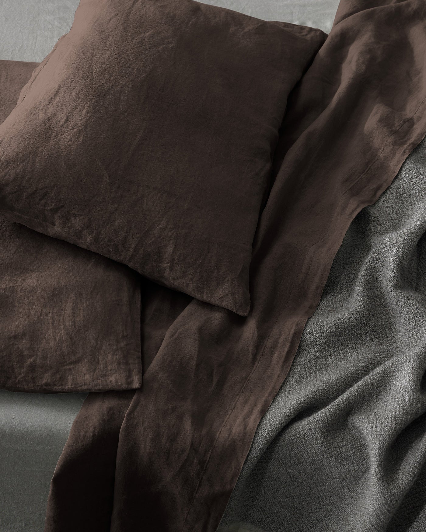 Close-up of Society Limonta Rem pillowcases in deep chocolate linen beside a slate coverlet.