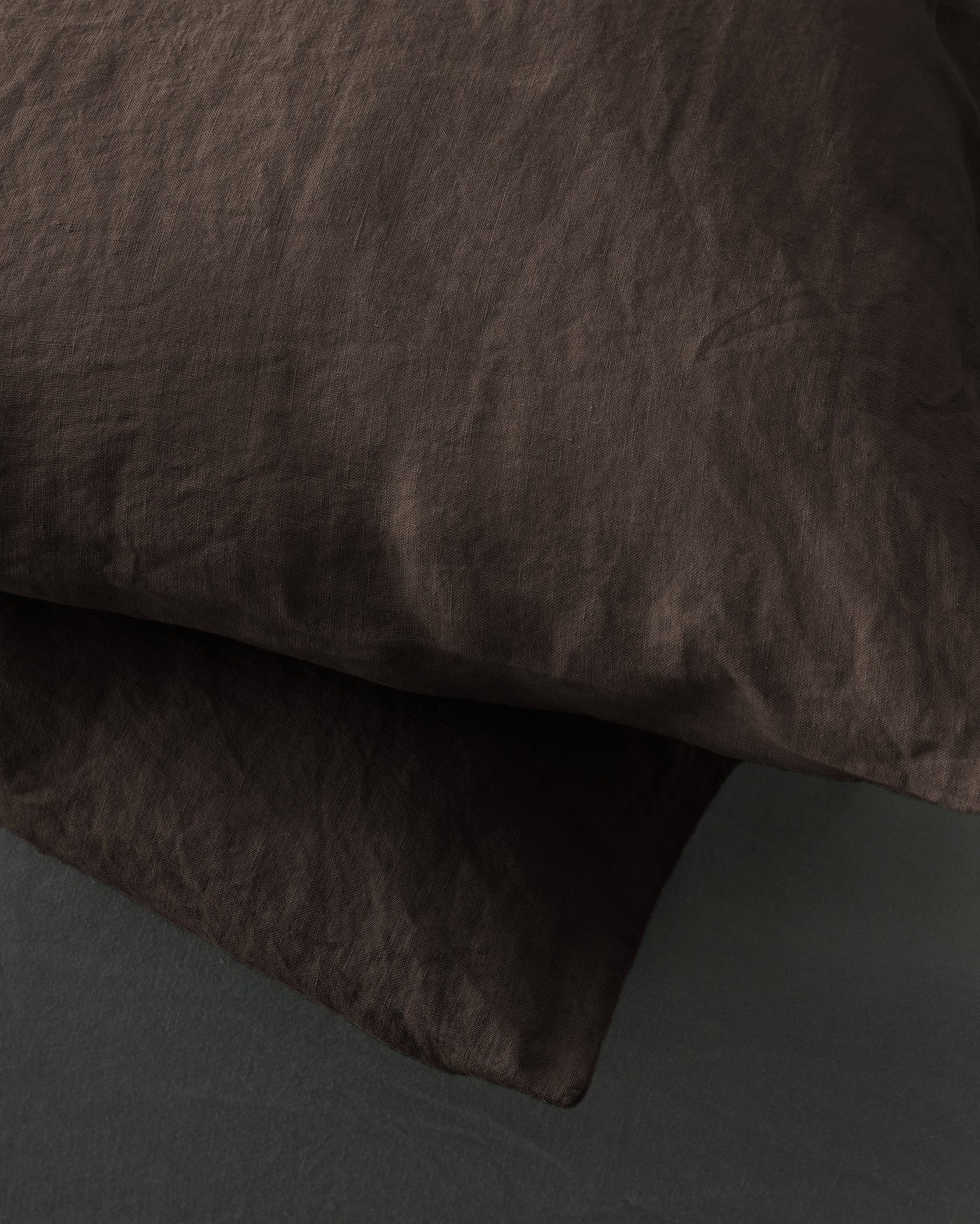 Close-up of washed linen pillowcase hem detail in deep espresso brown.