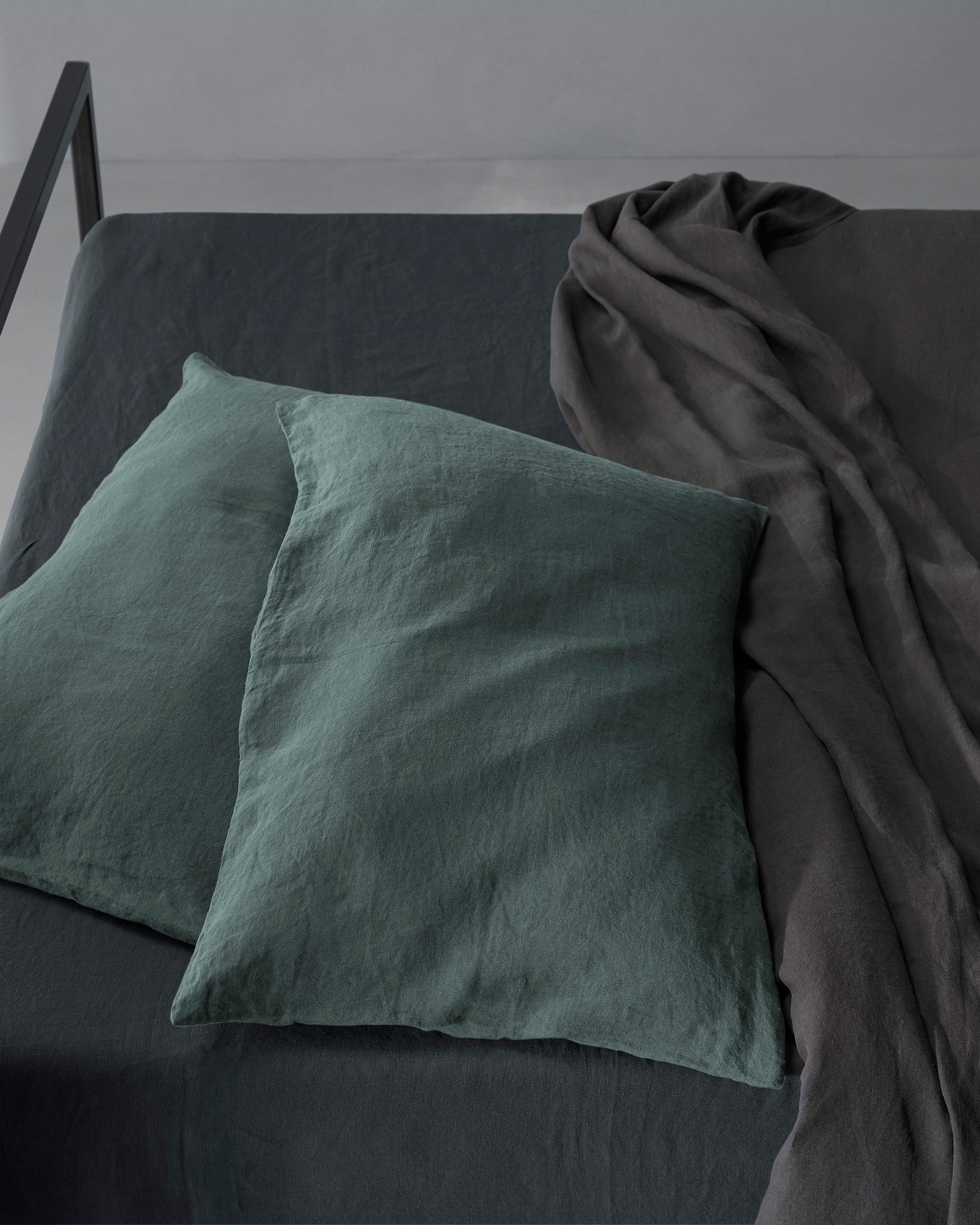 Forest green linen pillowcases styled against charcoal bedding, overhead angle.