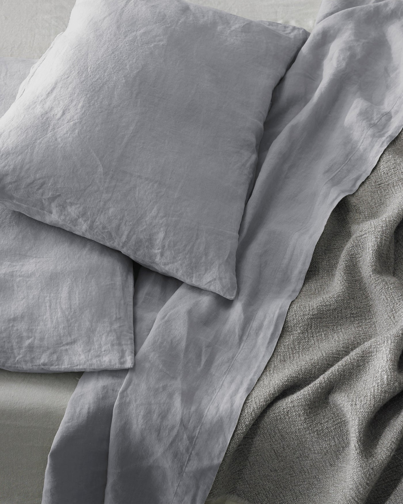 Close-up of Society Limonta Rem pillowcases in dove grey washed linen on a made bed.