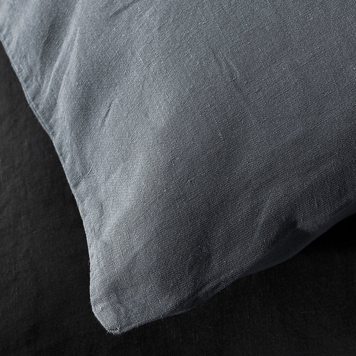 Close-up of Society Limonta Rem pillowcase corner in slate linen against dark bedding.
