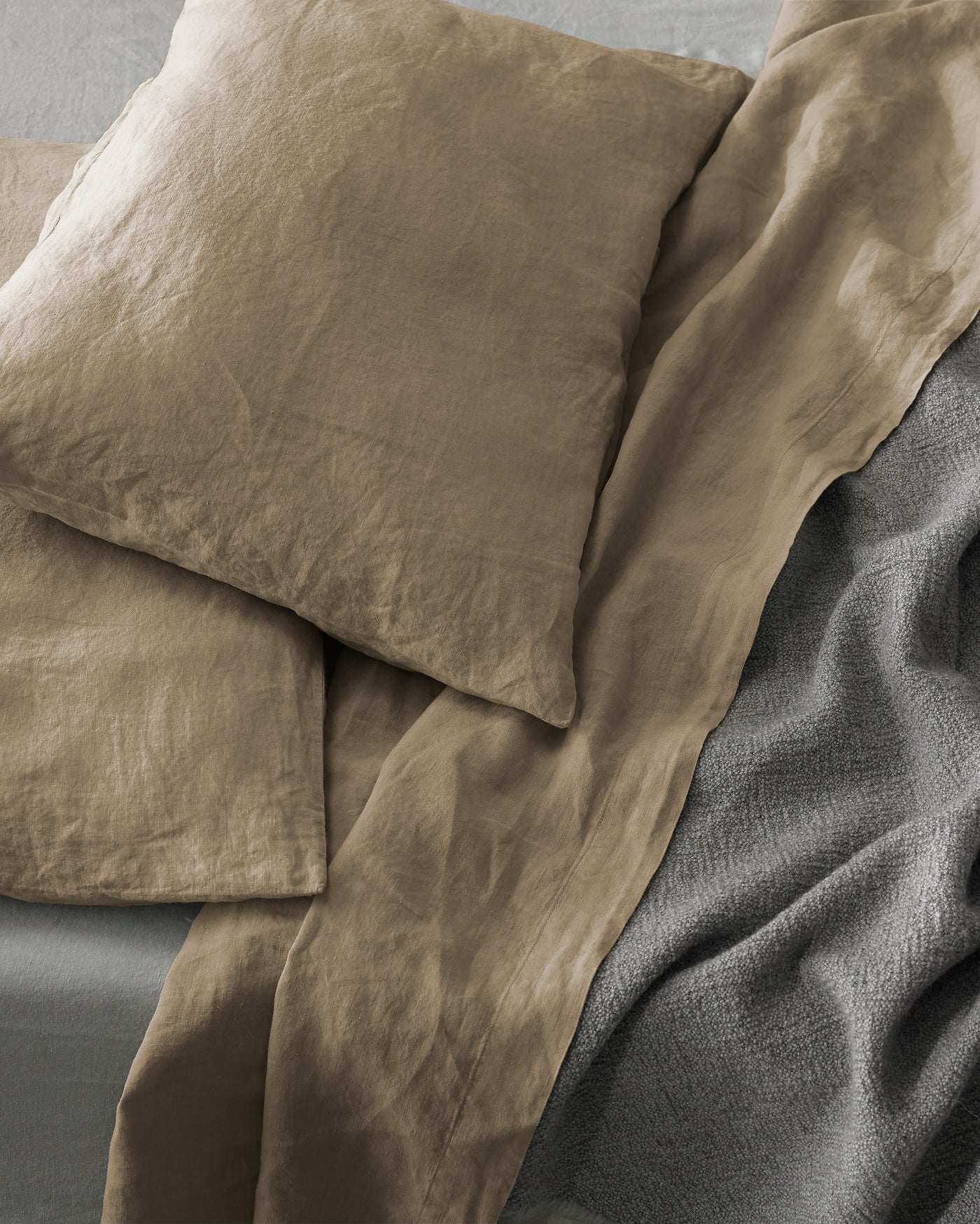 Close-up of Society Limonta Rem pillowcases in warm taupe washed linen, styled with a charcoal throw.