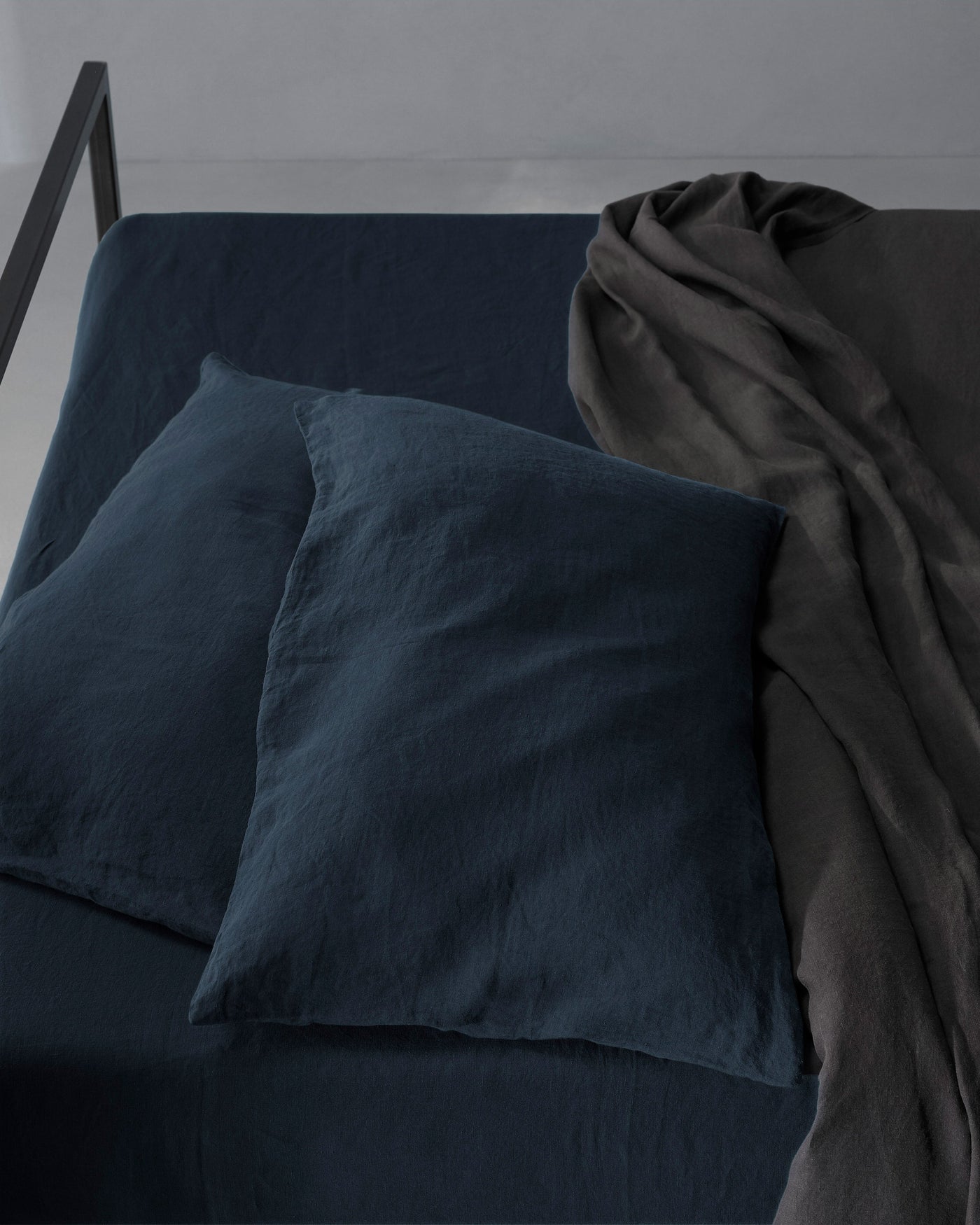 Society Limonta Rem pillowcases in midnight blue linen, overhead angle with charcoal throw draped alongside.