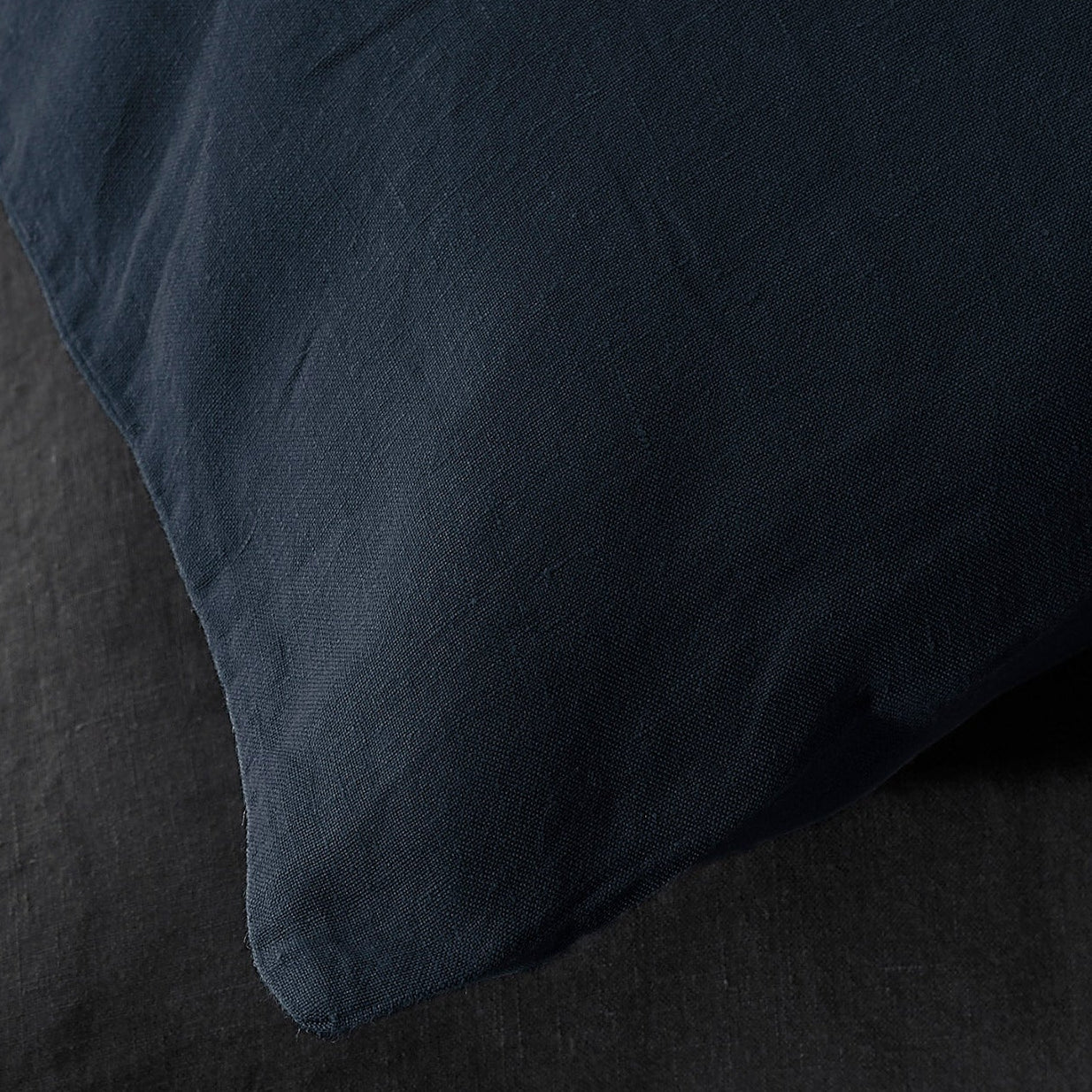 Close-up of navy linen pillowcase corner showing relaxed texture against charcoal bedding.