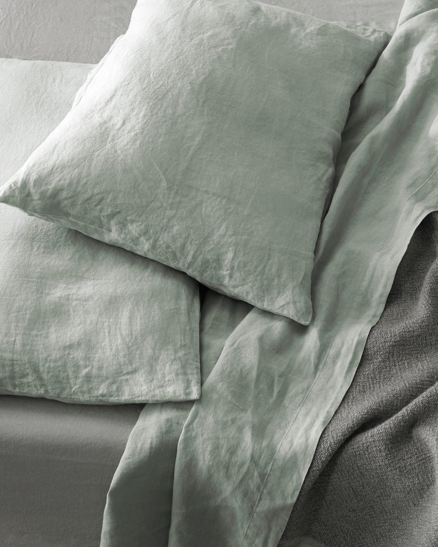Close-up of sage green washed linen pillowcases stacked, showing relaxed texture and soft drape.
