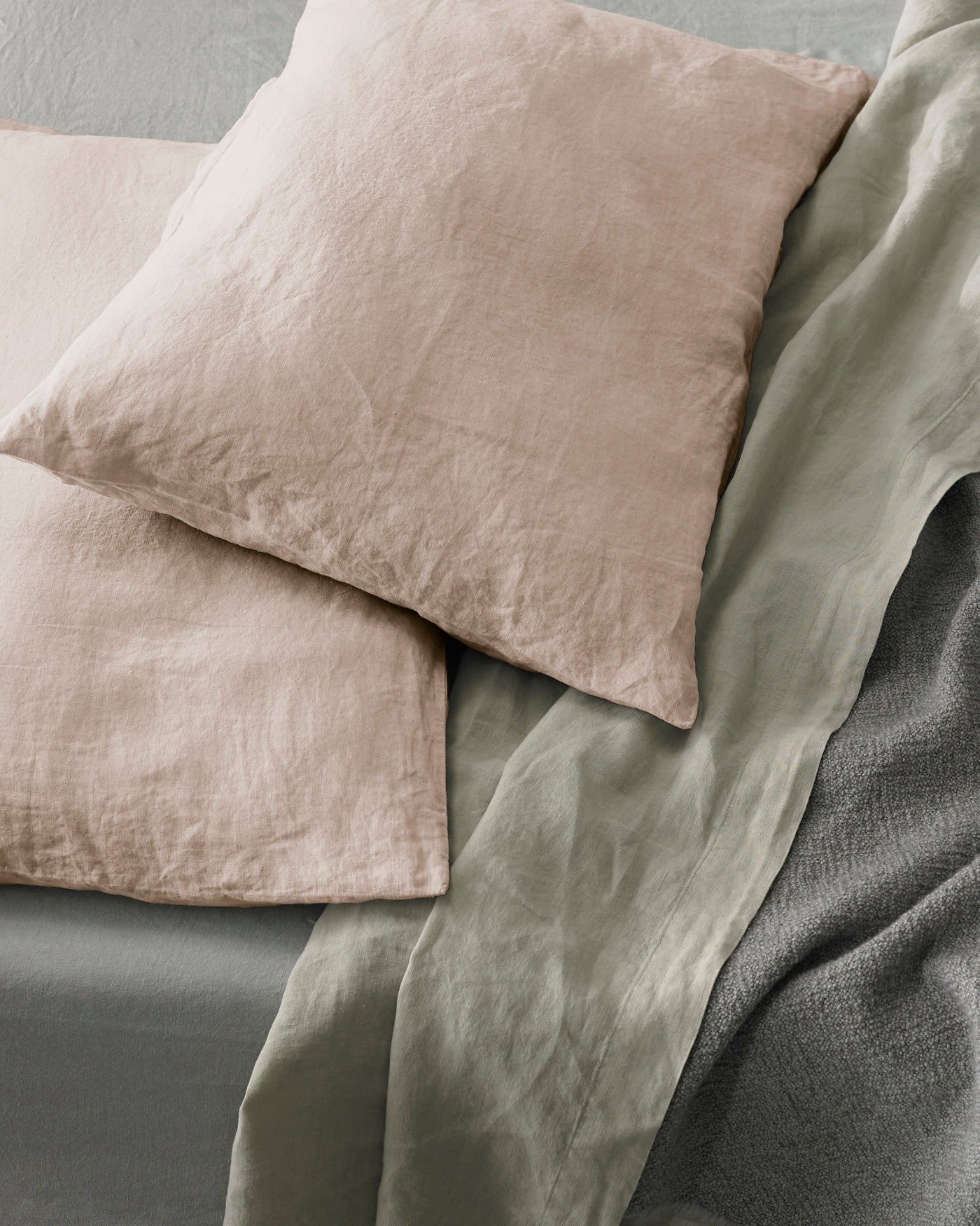 Close-up of blush linen pillowcases layered on sage and slate bedding.