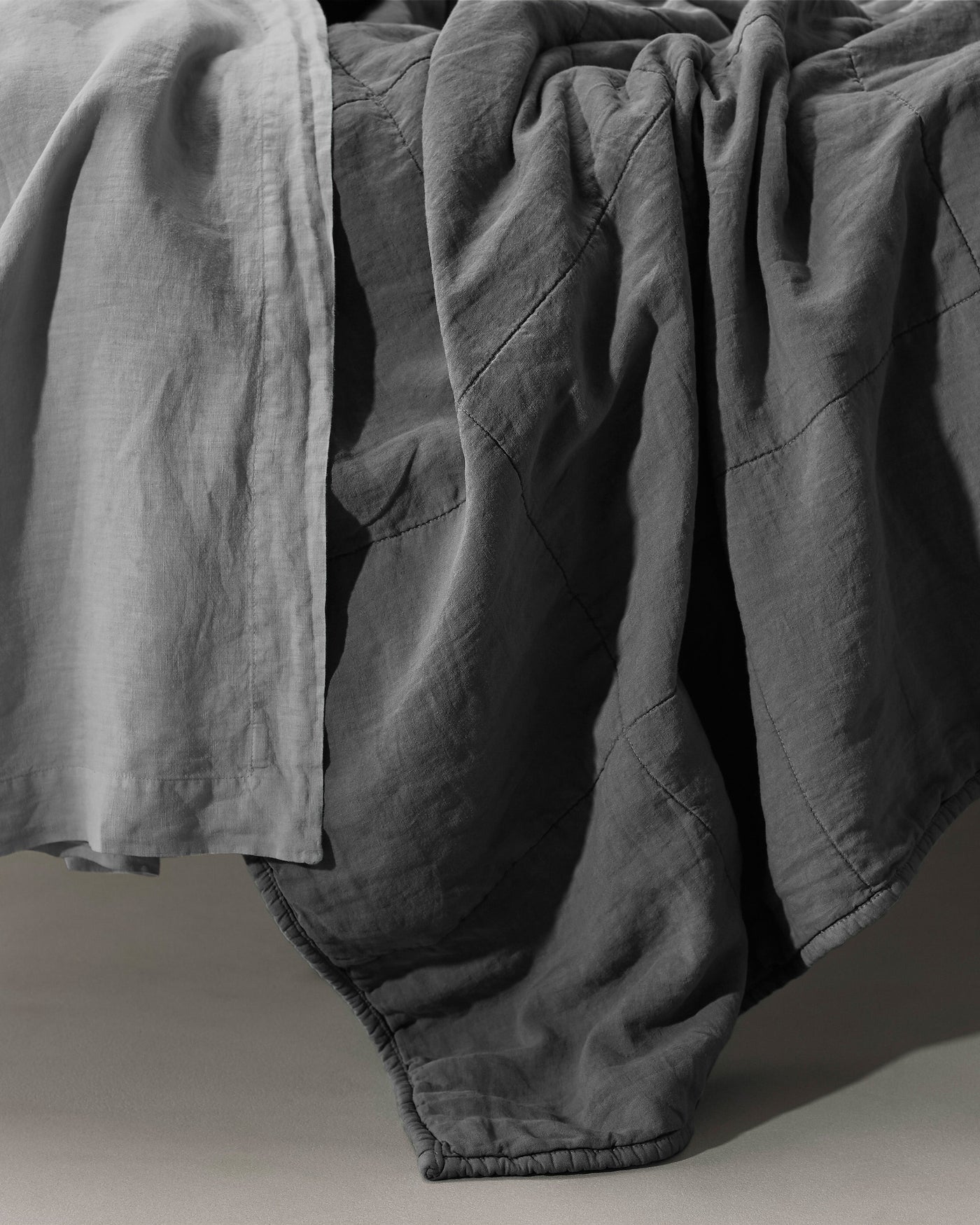 Close-up of slate linen quilt with visible stitched panel seams and draped texture.