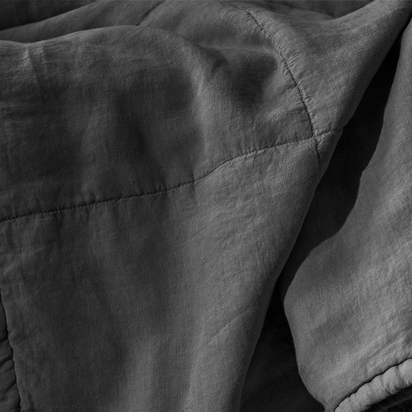 Close-up of charcoal linen quilt showing diamond quilting stitches and draped texture.