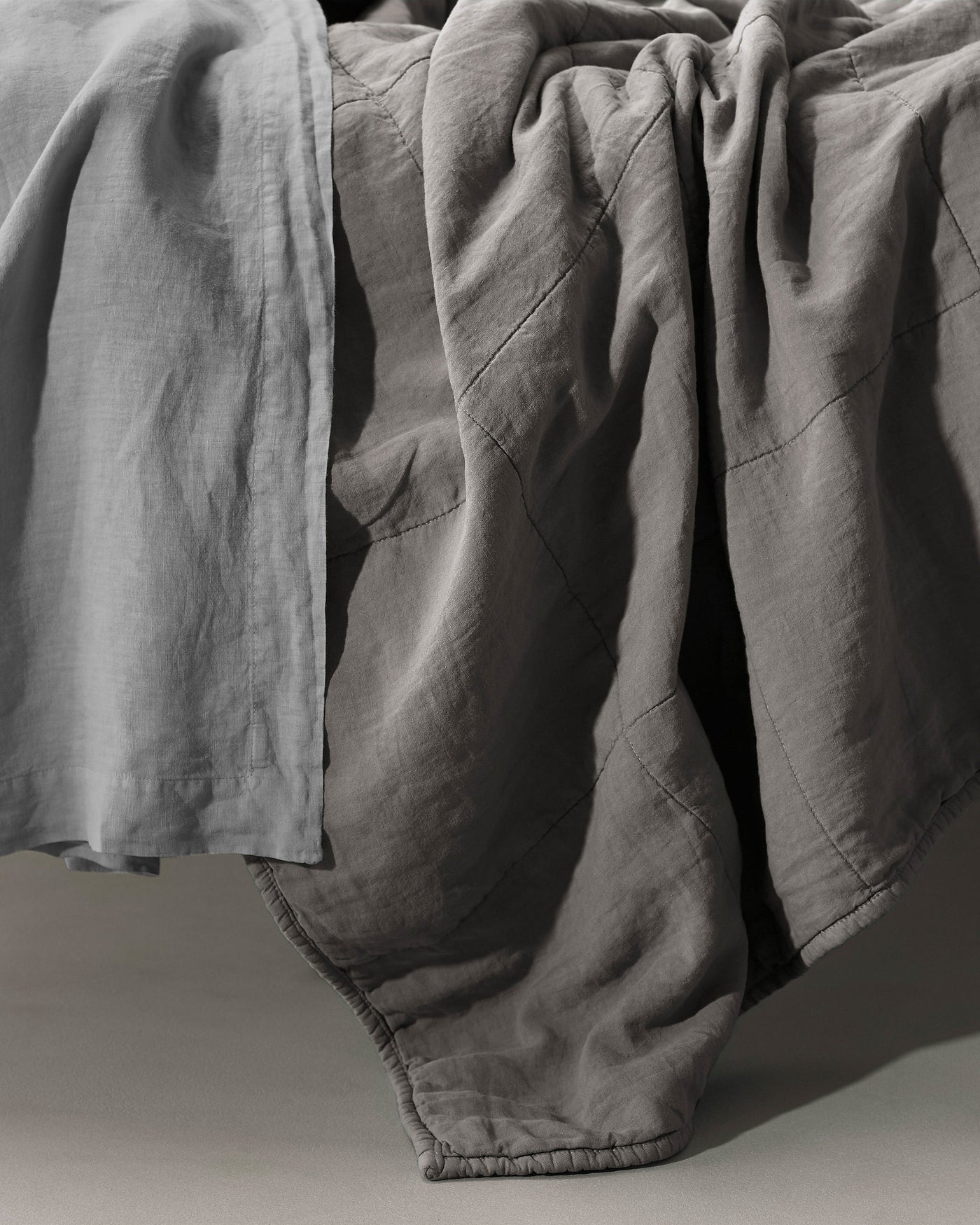 Close-up of Society Limonta Rem quilt in slate linen, showing diagonal quilting seams and draped texture.