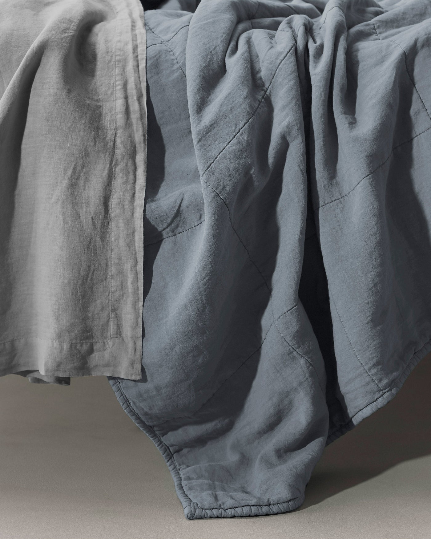 Society Limonta Rem linen quilt in slate blue with soft drape over bed edge.