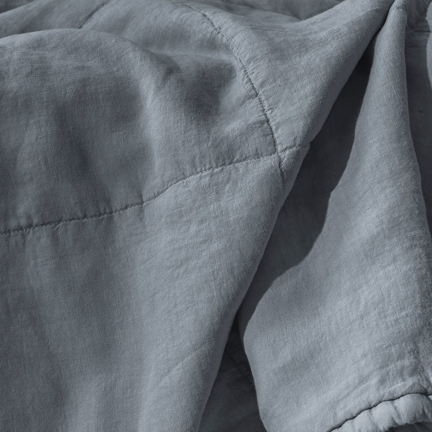 Close-up of Society Limonta Rem quilt in slate blue, showing diamond stitching and rumpled linen texture.