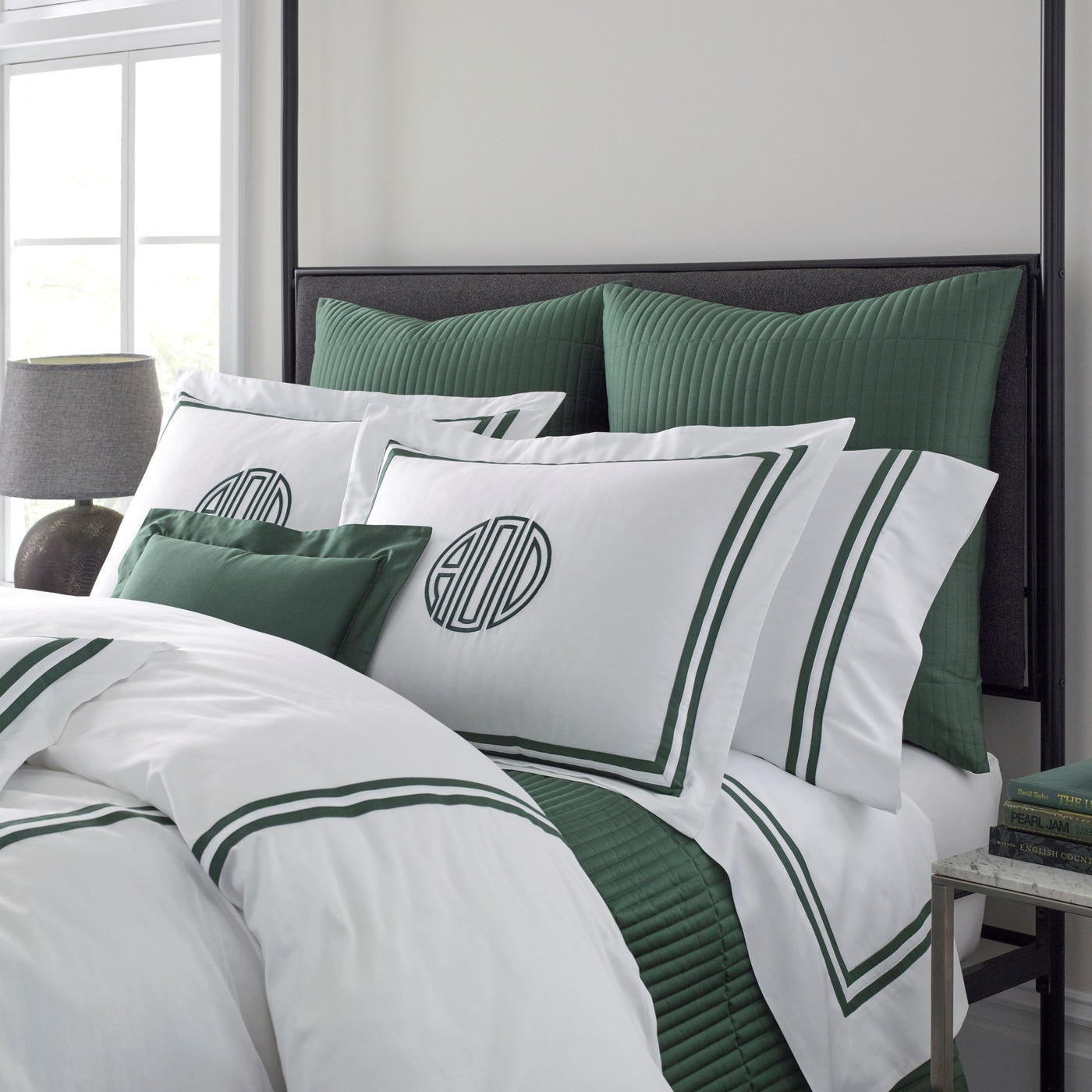 White cotton bedding with forest green ribbon border trim and monogram embroidery, styled on bed.