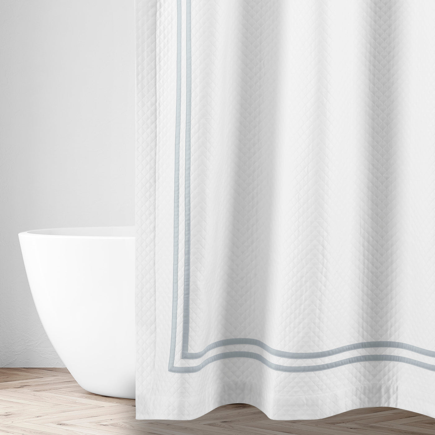 White matelassé shower curtain with silver-blue ribbon border trim, styled in a bathroom.