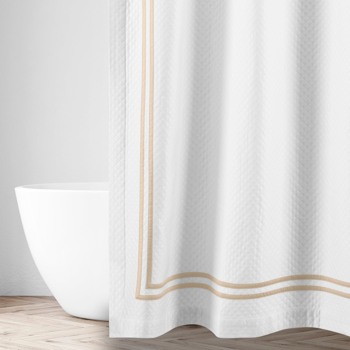 White matelassé shower curtain with champagne double-border trim, draped beside a freestanding tub.
