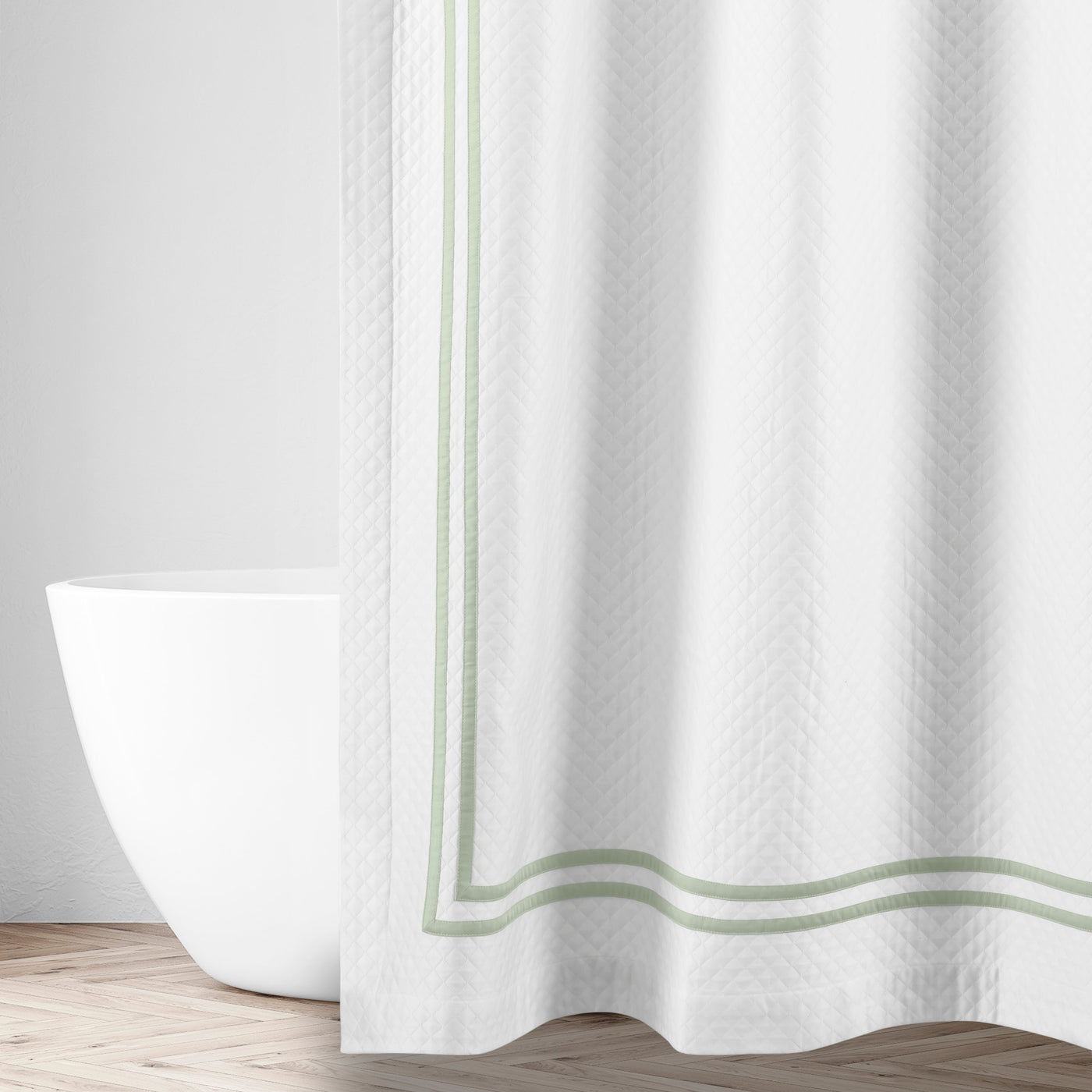 White matelassé shower curtain with sage double-stripe border, styled in a bright bathroom.