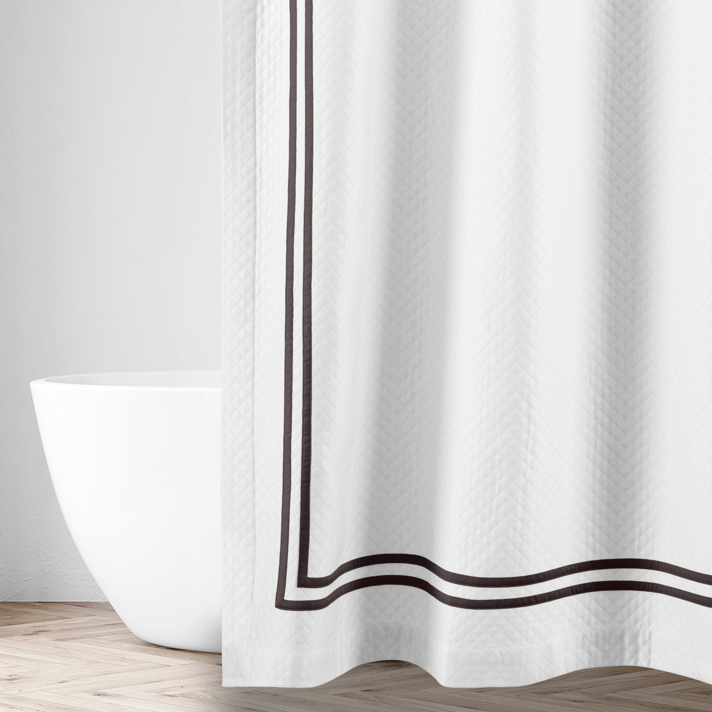 White matelassé shower curtain with double espresso satin border, styled in a bright bathroom.