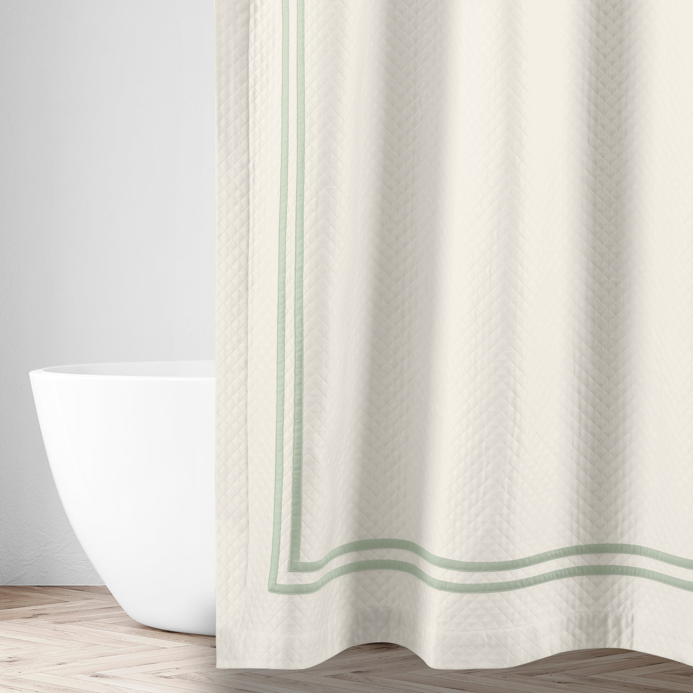 Ivory matelassé shower curtain with sage double-stripe border, draped in a bathroom setting.