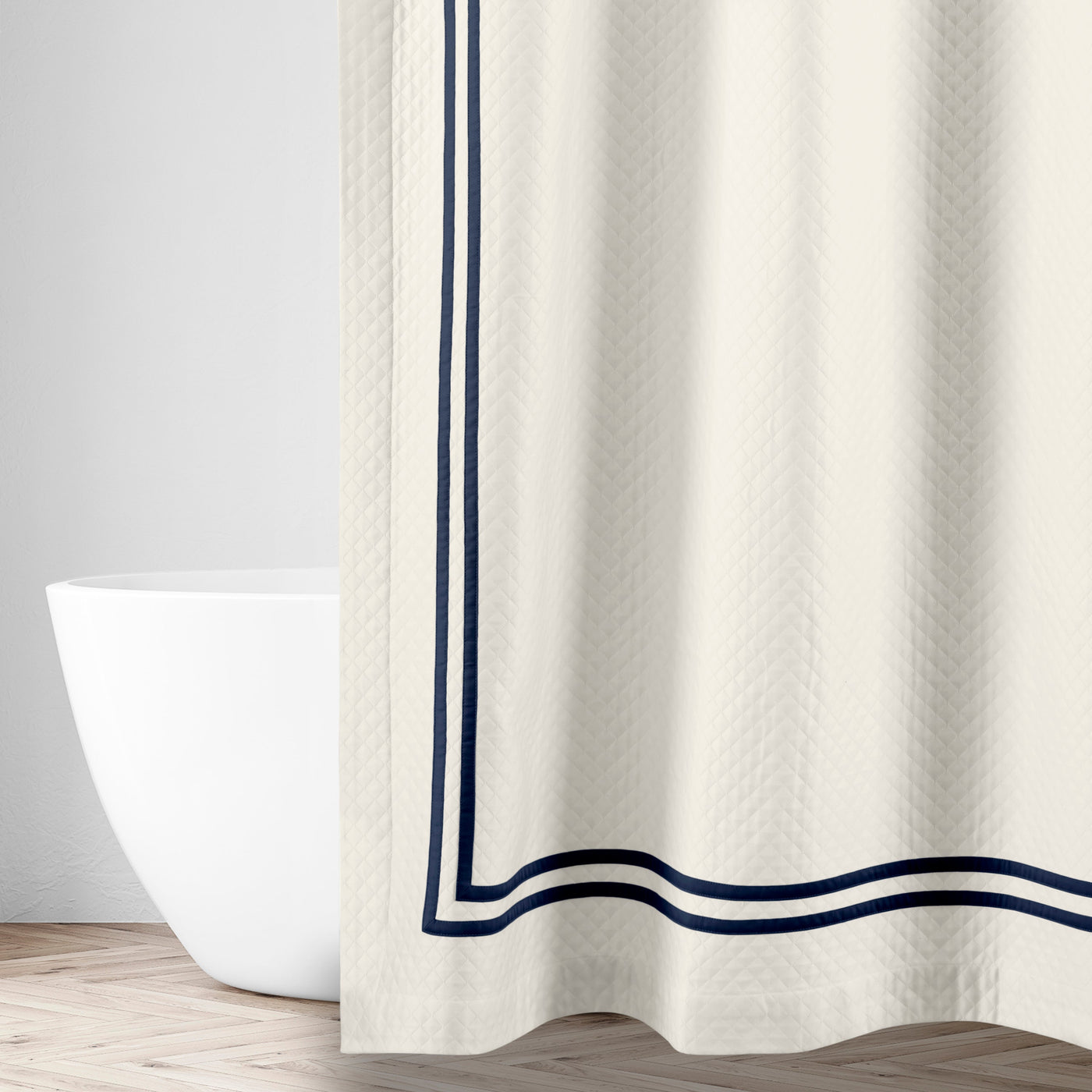 Ivory matelassé shower curtain with navy double-stripe border, styled in a bathroom setting.