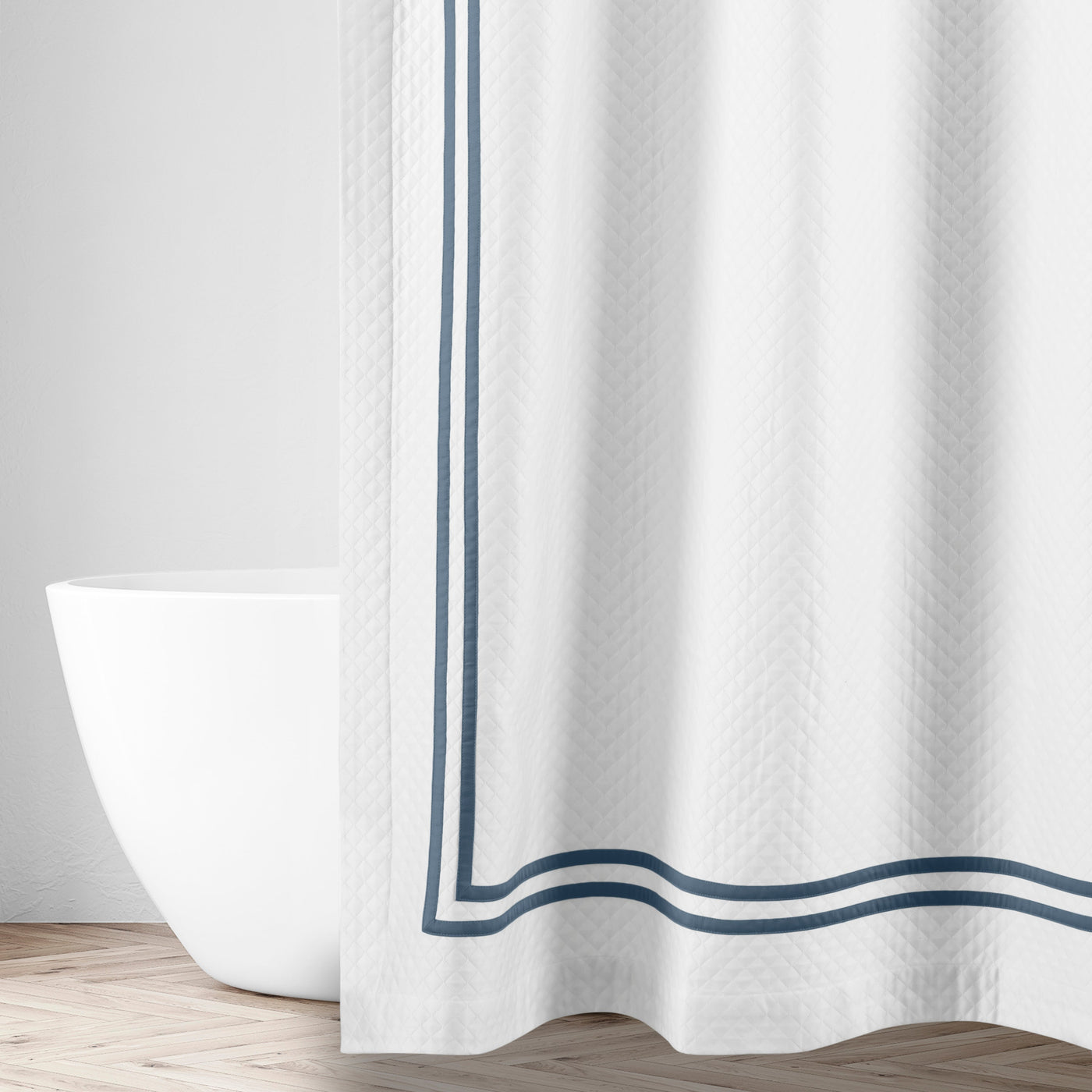 White matelassé shower curtain with double navy border trim, styled in a bright bathroom.
