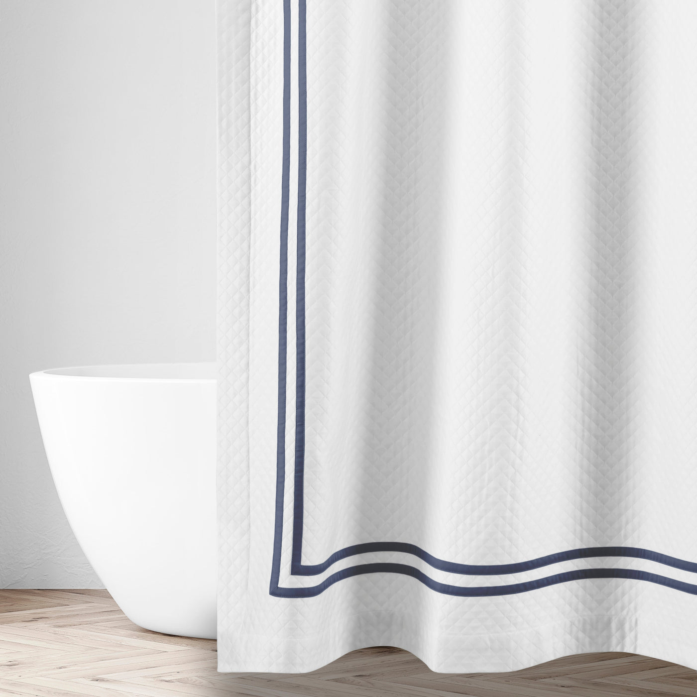 White matelassé shower curtain with navy double-border trim, styled in a bright bathroom.