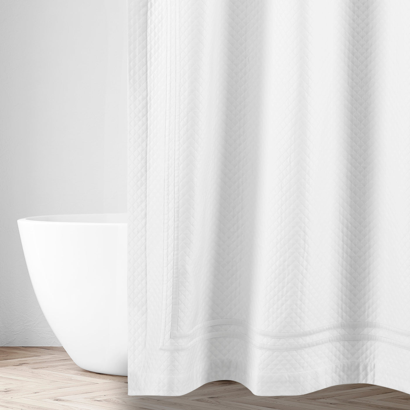 White cotton matelassé shower curtain with ribbon border, styled in a bright bathroom.