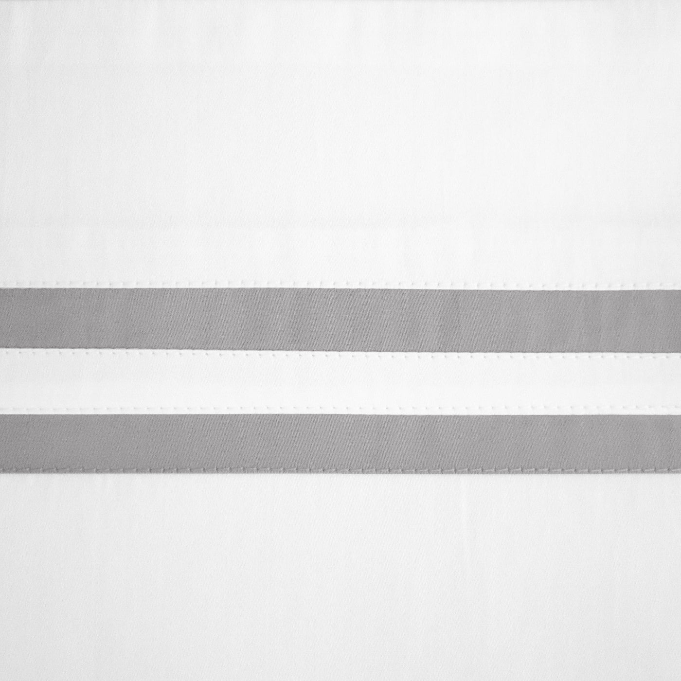 Close-up of white fabric with two parallel silver ribbon stripes and stitched edges.