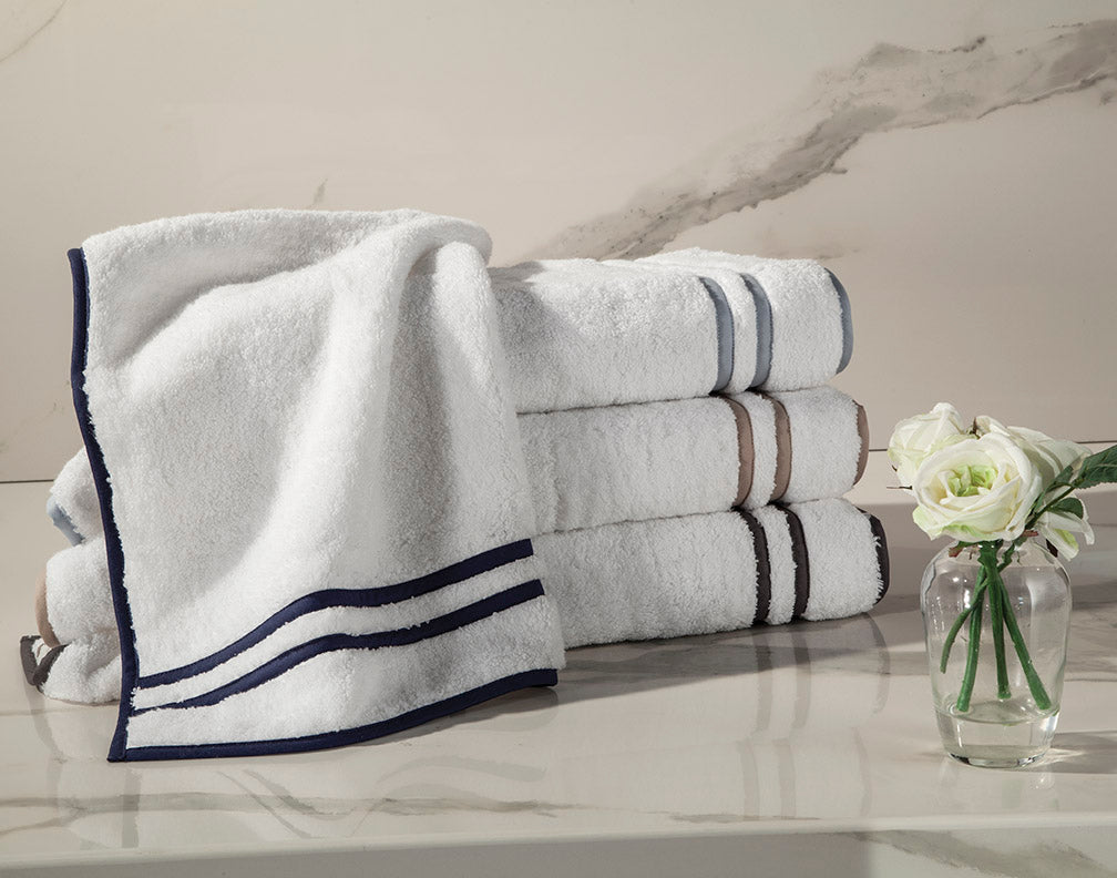 Close-up of white cotton towels with navy double-stripe border, stacked on marble surface.