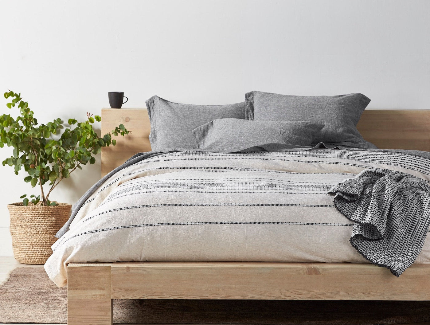 Ivory duvet cover with grey rippled stripes on a natural wood bed, styled with charcoal pillows.