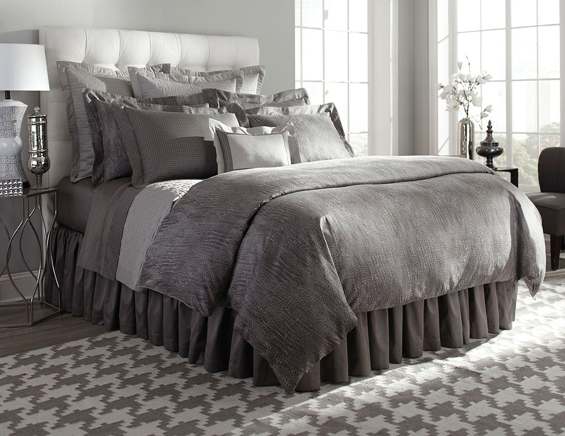 Charcoal Roberto bedding set styled on bed with layered grey pillows and ruffled bed skirt.