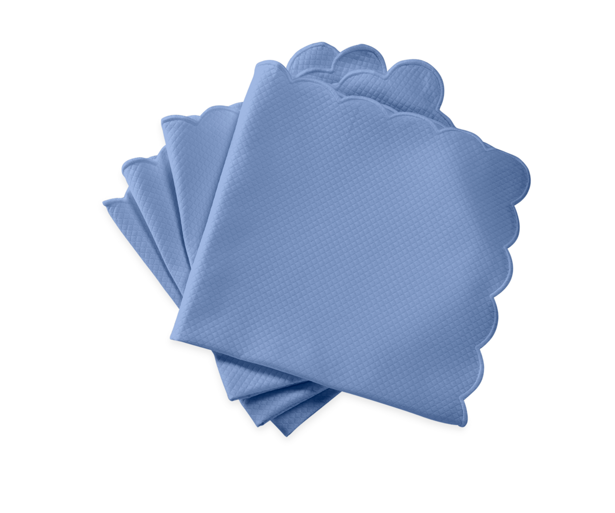 The Matouk Savannah Gardens Napkin Set features four blue, scalloped-edge, easy-care table linens, neatly stacked on a light background.