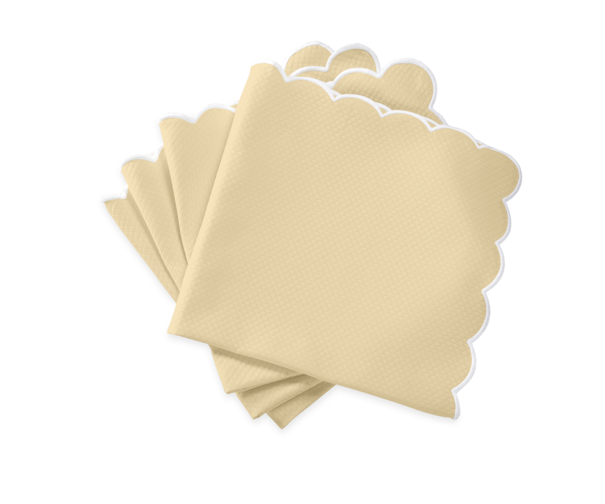Five beige Savannah Gardens napkins by Matouk, featuring scalloped white edges, are fanned out on a white background—an elegant complement to diamond pique table linens.