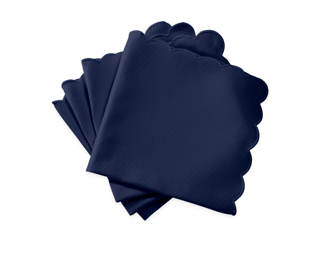 The Matouk Savannah Gardens Napkin Set features four navy blue napkins with scalloped edges, fanned out on a white background—ideal for pairing with easy-care table linens for effortless elegance.