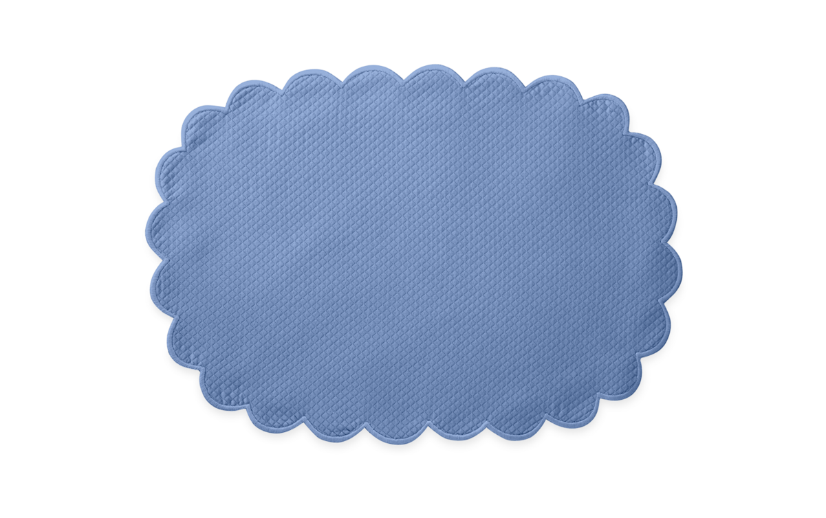 A blue, oval placemat with a diamond pique texture and scalloped edges from the Matouk Savannah Gardens collection, shown on a plain white background.