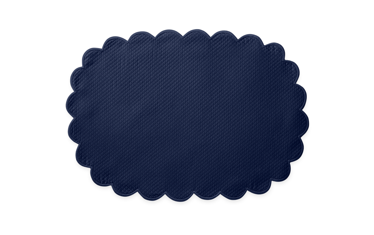 The Matouk Savannah Gardens Placemat Set features dark blue, oval placemats with a scalloped edge and diamond pique texture, displayed on a plain light background.