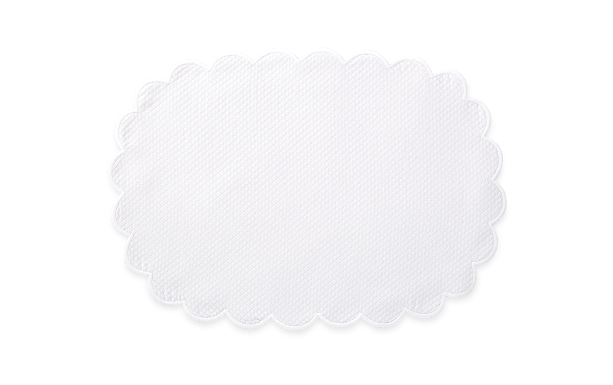 The Savannah Gardens Placemat Set by Matouk features an oval white design with a scalloped edge and the brand’s signature diamond pique, set against a plain light background.
