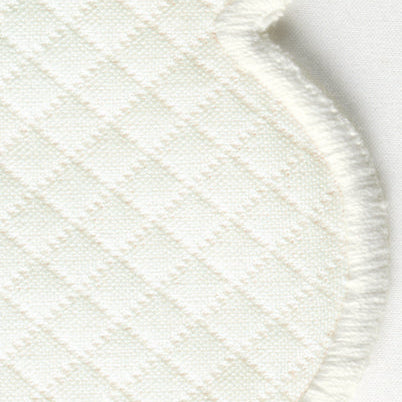 Closeup of Savannah Gardens | Napkin Set by Matouk shows white quilted fabric with a diamond pattern and a scalloped, frayed edge, reminiscent of diamond pique table linens, against a plain background.