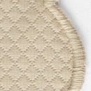 Close-up of a beige carpet with a diamond pattern and rounded, stitched edge, reminiscent of the elegant textures in Matouk’s Savannah Gardens Napkin Set.
