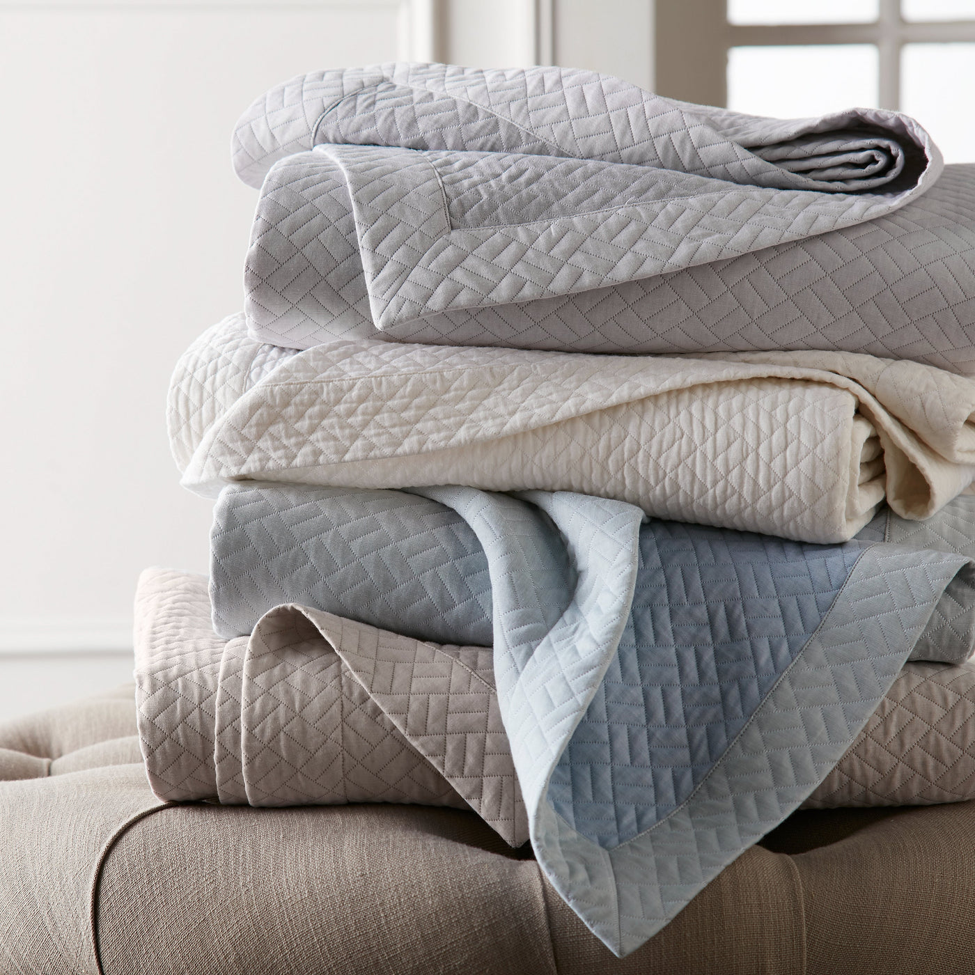 Home Treasures Savannah quilted coverlets stacked in grey, ivory, and blue.