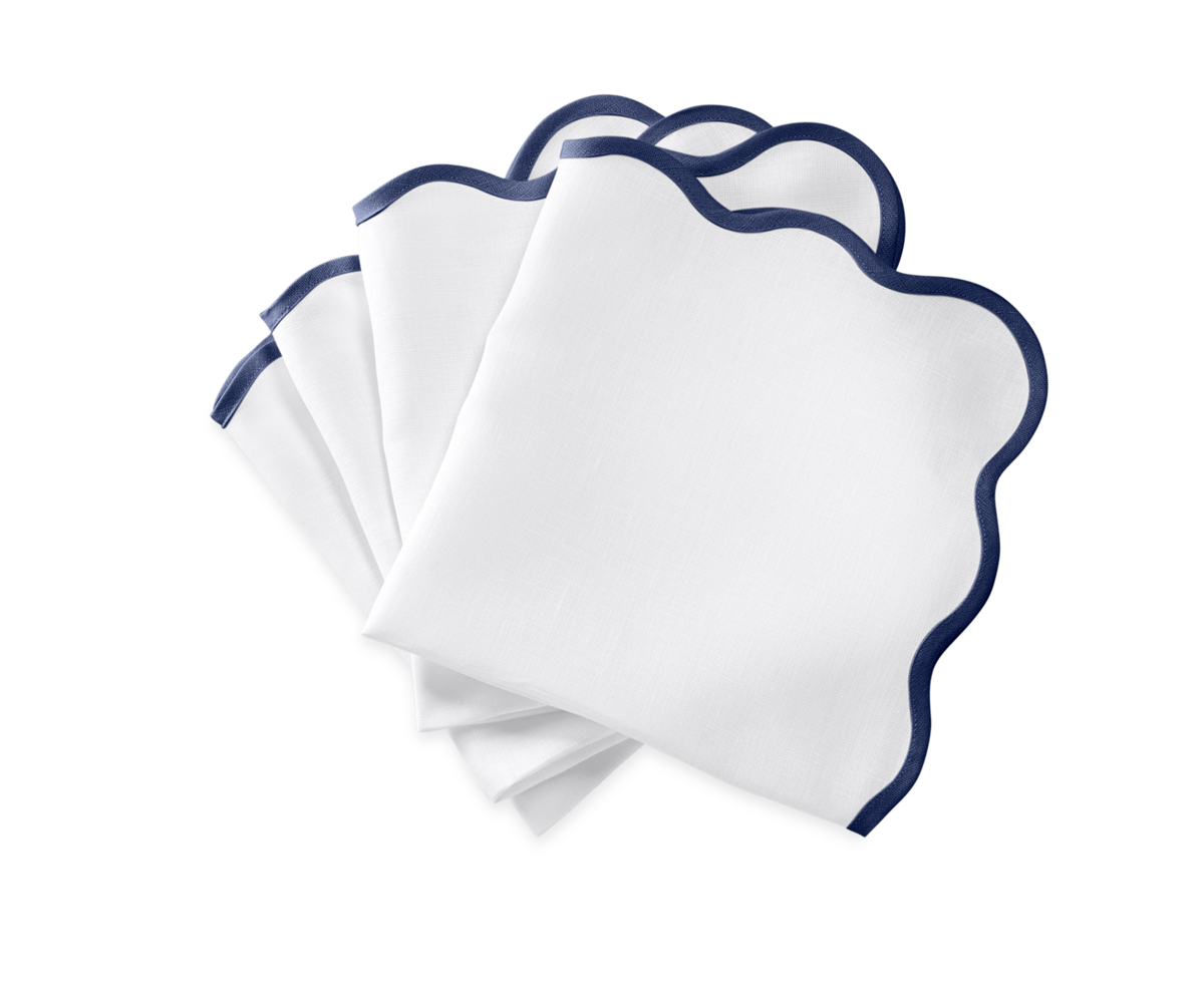 The Matouk Scallop Edge | Napkin Set features four white napkins with dark blue trim, fanned out on a plain background to bring refined elegance to any tablescape.