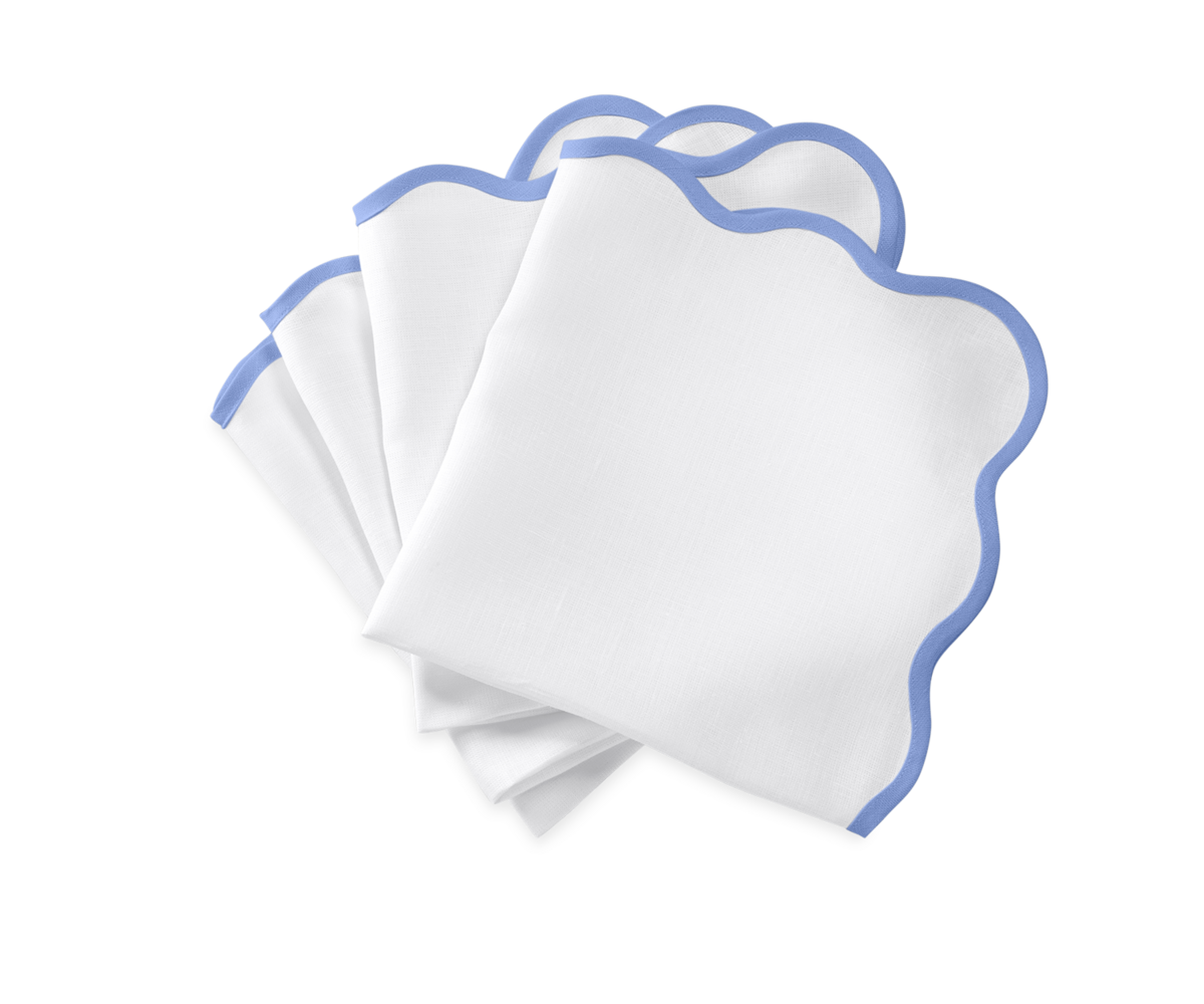 The Matouk Scallop Edge Napkin Set features four white napkins with light blue trim, fanned on a white background—ideal for elevating any tablescape or pairing with your favorite linen placemats.