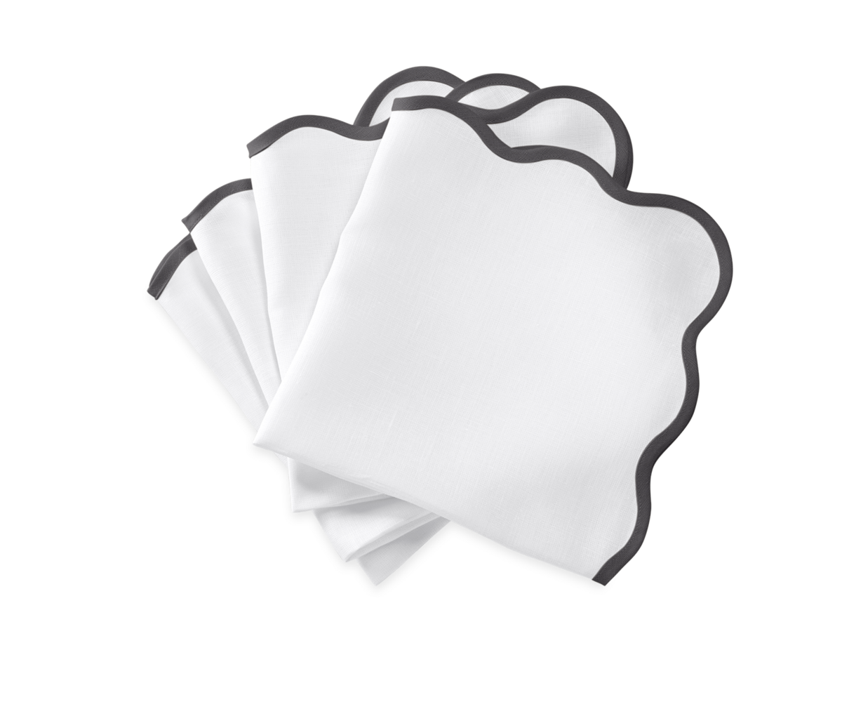 The Matouk Scallop Edge | Napkin Set features four white napkins with wavy edges and black trim—perfect for elevating your tablescape or pairing with your favorite linen placemats.
