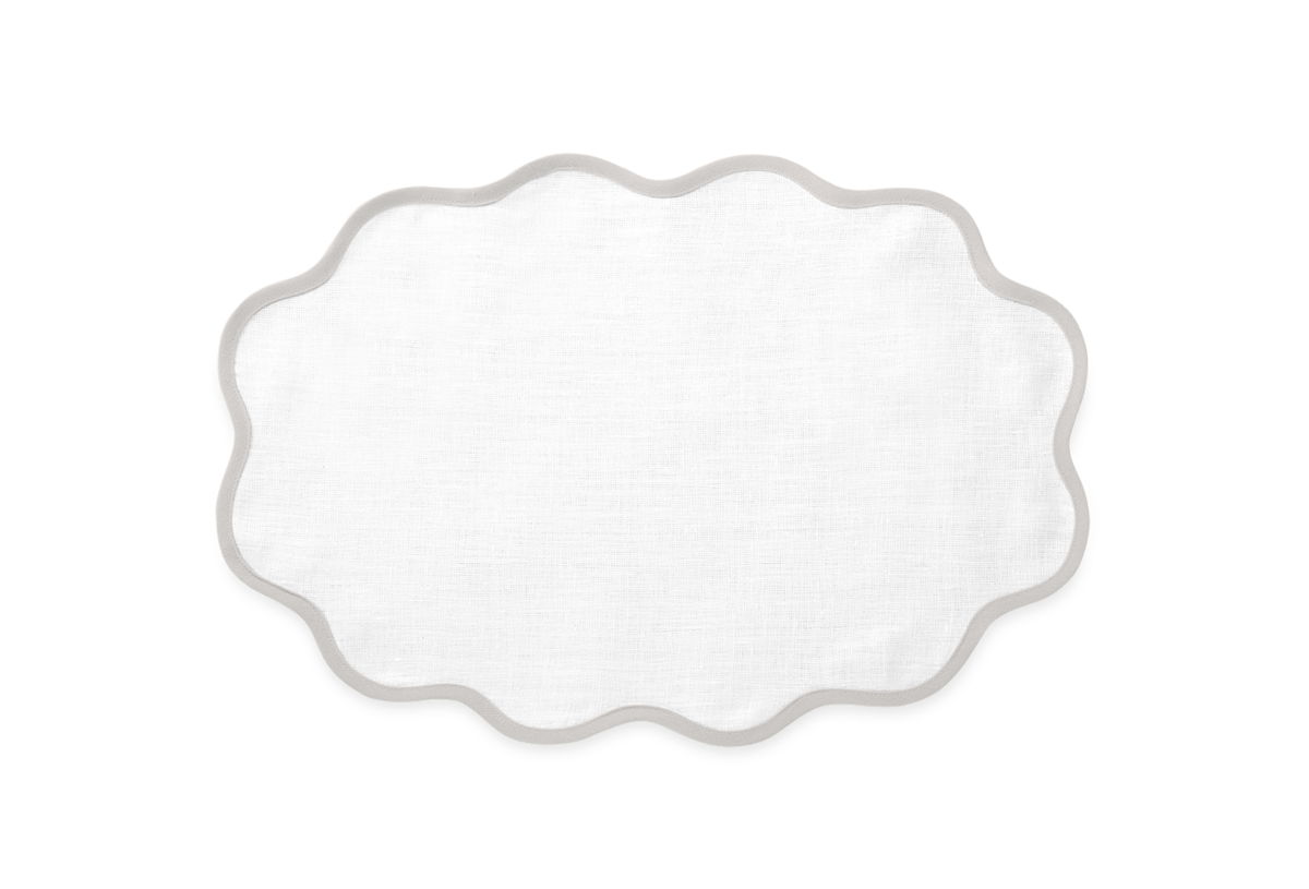 The Matouk Scallop Edge Placemat Set features white oval linen placemats with scalloped edges and light grey trim, perfect for a unique tablescape. Shown on a plain white background.